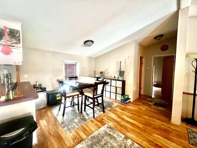 dining room featuring a textured ceiling, vaulted ceiling, and wood-type flooring