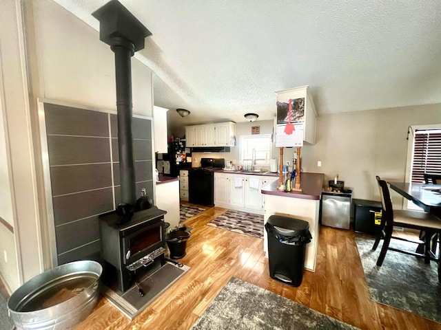 kitchen with sink, light hardwood / wood-style flooring, a wood stove, black gas stove, and white cabinets