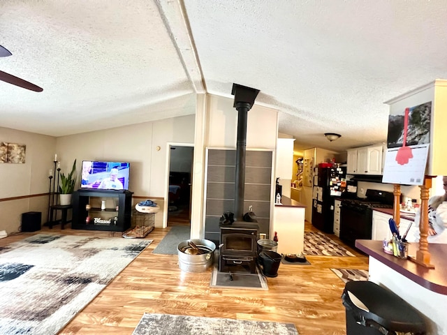 living room featuring a textured ceiling, light hardwood / wood-style floors, a wood stove, vaulted ceiling, and ceiling fan