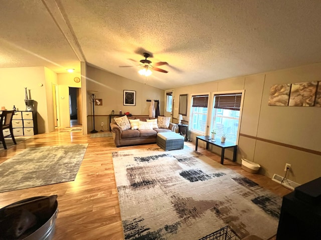 living room featuring light hardwood / wood-style flooring, a textured ceiling, vaulted ceiling, and ceiling fan