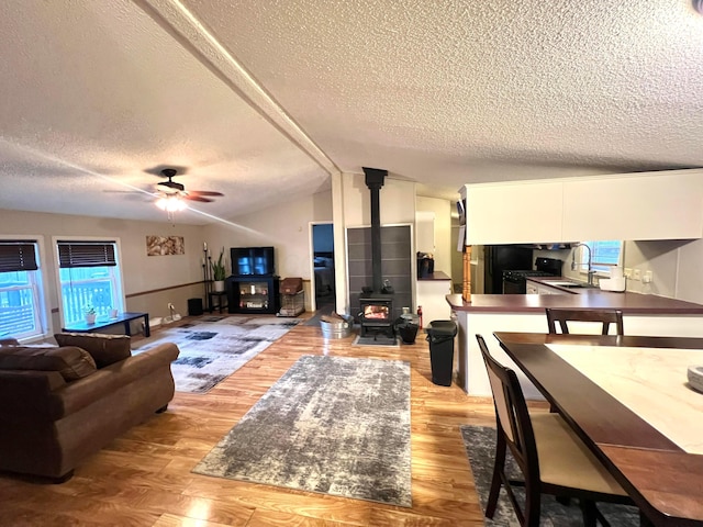 living room featuring lofted ceiling, sink, ceiling fan, light hardwood / wood-style floors, and a wood stove