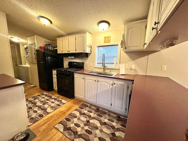 kitchen featuring sink, light hardwood / wood-style flooring, black appliances, white cabinets, and washer / dryer