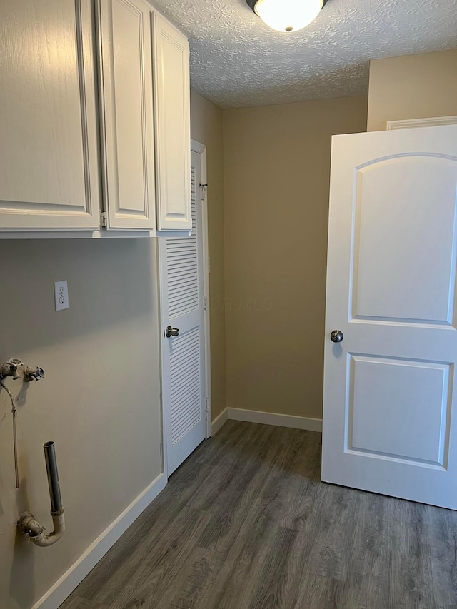 clothes washing area featuring cabinet space, dark wood finished floors, a textured ceiling, and baseboards