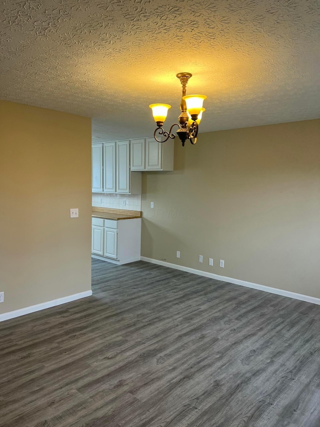 spare room featuring a chandelier, a textured ceiling, dark wood finished floors, and baseboards