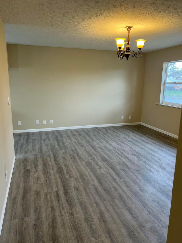 empty room with a notable chandelier, a textured ceiling, baseboards, and dark wood-type flooring