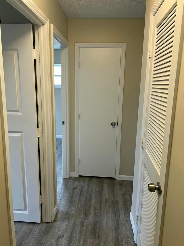 hallway with dark wood-type flooring, a textured ceiling, and baseboards