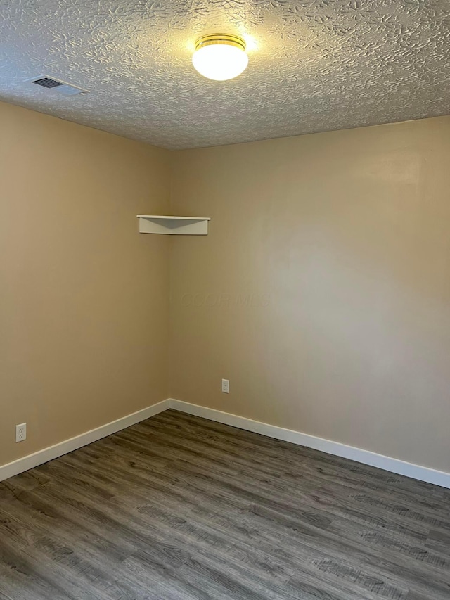 empty room with dark wood-style floors, visible vents, a textured ceiling, and baseboards