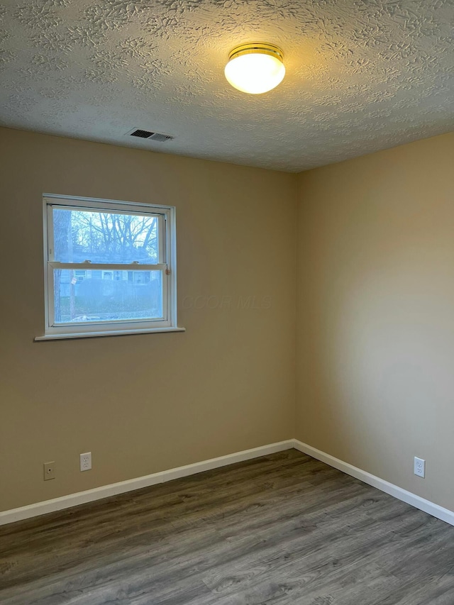 spare room with dark wood-style floors, baseboards, visible vents, and a textured ceiling