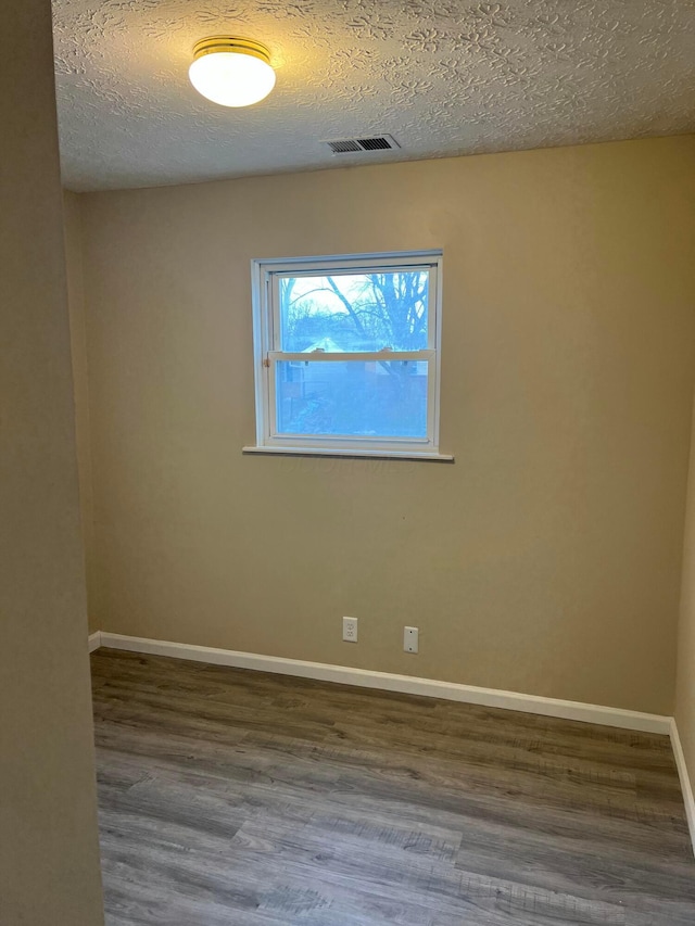 spare room with a textured ceiling, wood finished floors, visible vents, and baseboards