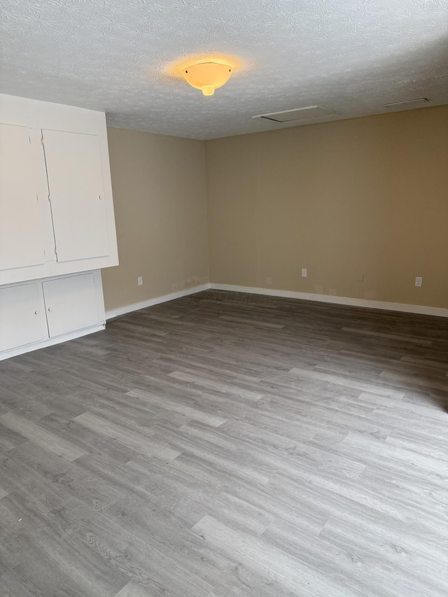 empty room with light wood-style floors, visible vents, a textured ceiling, and baseboards