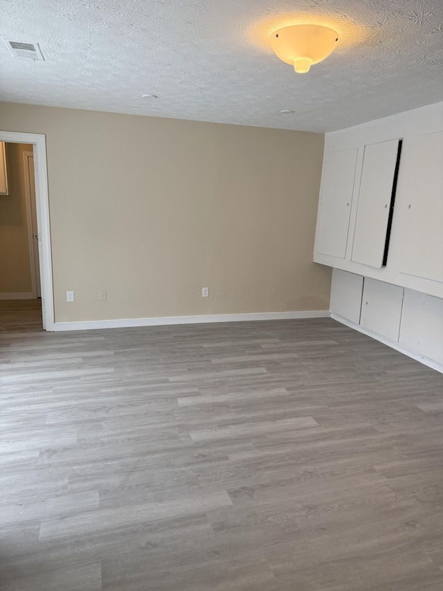 spare room with baseboards, light wood-style flooring, visible vents, and a textured ceiling