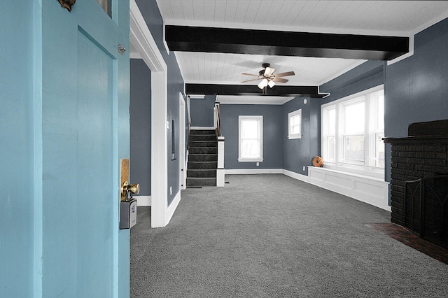 unfurnished living room featuring beam ceiling, a fireplace, ceiling fan, and dark colored carpet