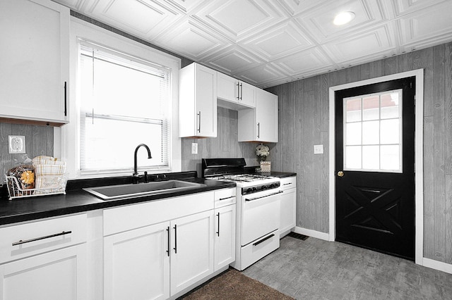 kitchen with sink, gas range gas stove, wood walls, white cabinetry, and light wood-type flooring