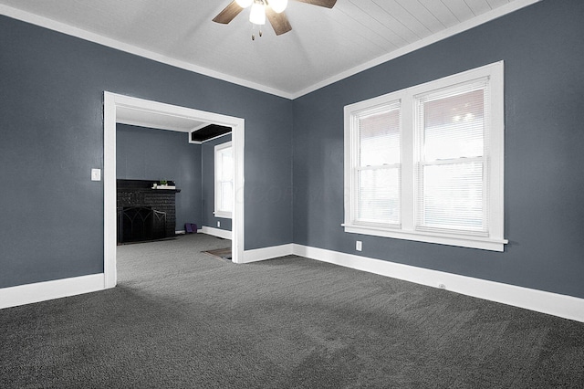 unfurnished room with crown molding, ceiling fan, a fireplace, and dark colored carpet