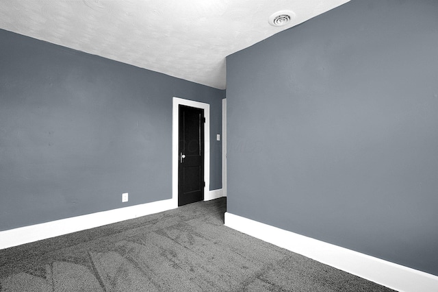 spare room featuring dark carpet and a textured ceiling