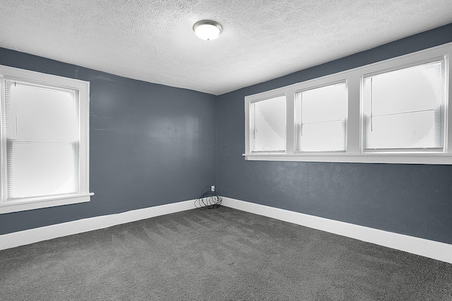 spare room featuring dark carpet, plenty of natural light, and a textured ceiling