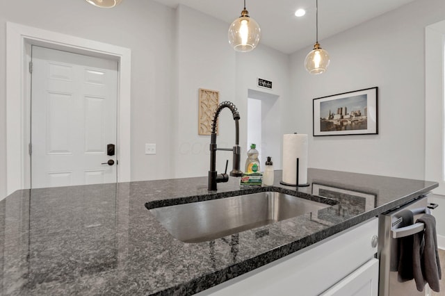 kitchen with sink, dark stone countertops, white cabinetry, and hanging light fixtures