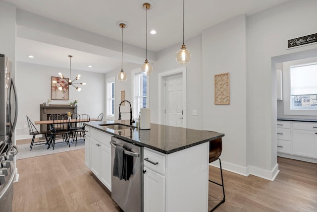 kitchen featuring a kitchen island with sink, white cabinets, sink, appliances with stainless steel finishes, and a breakfast bar area