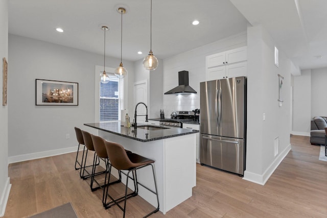 kitchen with a center island with sink, sink, wall chimney exhaust hood, appliances with stainless steel finishes, and white cabinetry