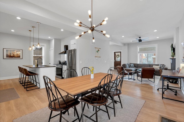 dining area with ceiling fan with notable chandelier, light wood-type flooring, and sink