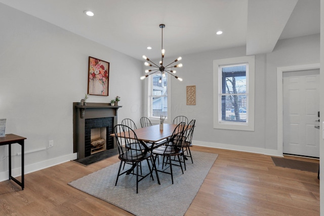 dining space with a fireplace, an inviting chandelier, and light hardwood / wood-style flooring