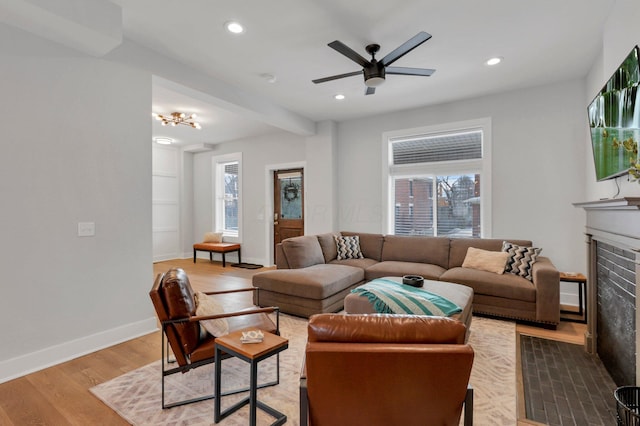 living room with ceiling fan, a healthy amount of sunlight, wood-type flooring, and a brick fireplace