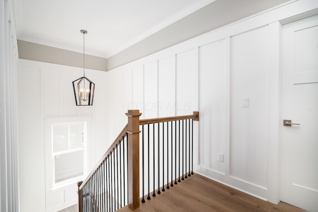 stairway featuring wood-type flooring, crown molding, and an inviting chandelier