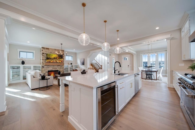 kitchen with wine cooler, a fireplace, a center island with sink, white cabinets, and appliances with stainless steel finishes