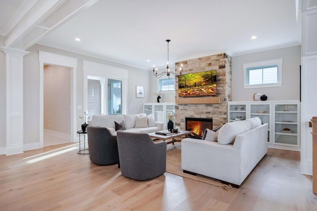 living room with crown molding, a fireplace, a notable chandelier, and light hardwood / wood-style flooring