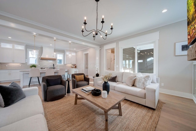 living room featuring an inviting chandelier, sink, crown molding, light hardwood / wood-style flooring, and decorative columns