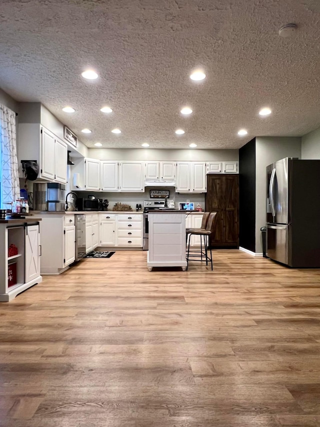 kitchen featuring white cabinets, appliances with stainless steel finishes, light wood-type flooring, and a textured ceiling