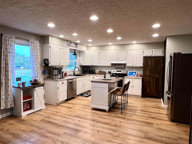 kitchen with a center island, white cabinets, light hardwood / wood-style flooring, appliances with stainless steel finishes, and a breakfast bar area