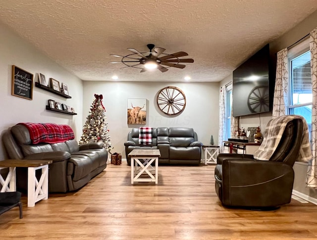 living room featuring ceiling fan, light wood-type flooring, and a textured ceiling