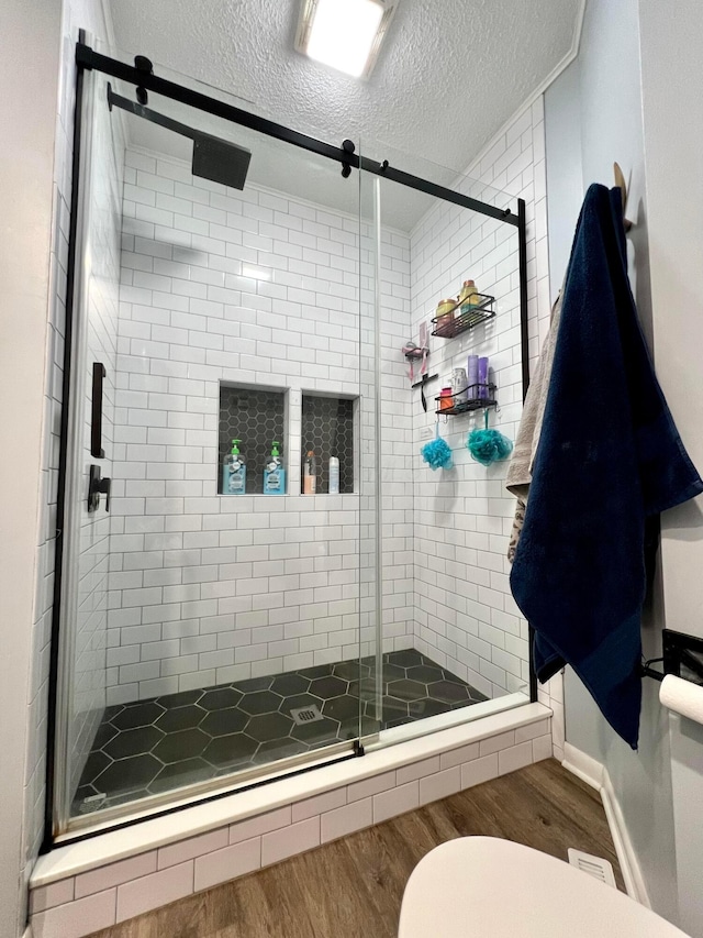 bathroom featuring wood-type flooring, a textured ceiling, toilet, and a shower with shower door