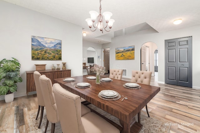 dining area with a notable chandelier, light wood-type flooring, and a textured ceiling