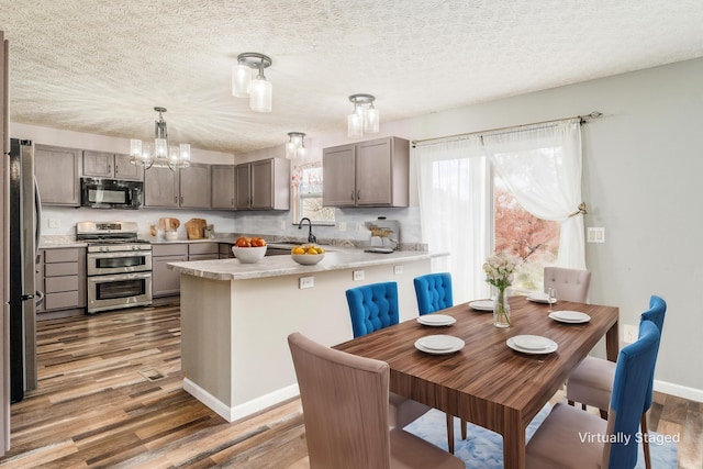 kitchen with kitchen peninsula, appliances with stainless steel finishes, gray cabinetry, dark hardwood / wood-style floors, and hanging light fixtures