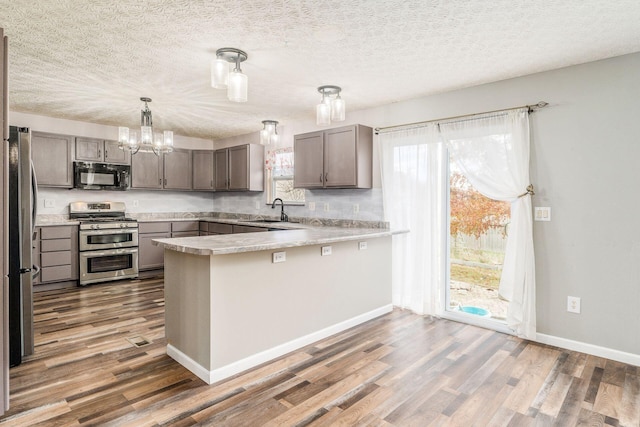 kitchen featuring sink, stainless steel appliances, dark hardwood / wood-style flooring, kitchen peninsula, and pendant lighting