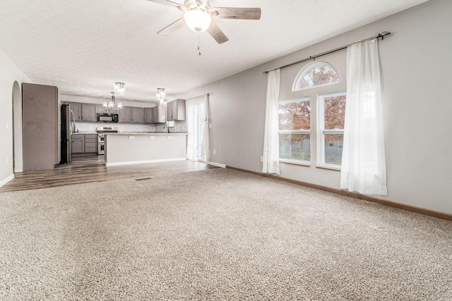 unfurnished living room with dark colored carpet, ceiling fan with notable chandelier, and a textured ceiling