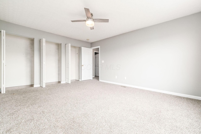 unfurnished bedroom featuring carpet flooring, ceiling fan, and two closets