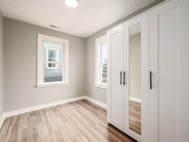 unfurnished bedroom with a textured ceiling, light hardwood / wood-style flooring, and multiple windows