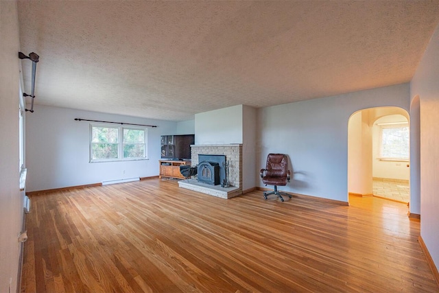 unfurnished living room with a wealth of natural light, a baseboard radiator, a textured ceiling, and light wood-type flooring