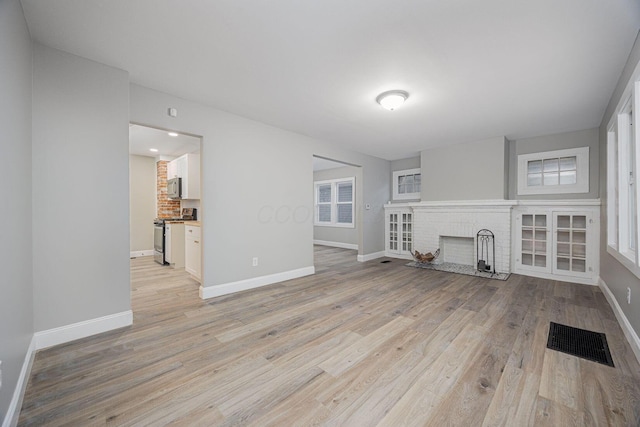 unfurnished living room featuring light hardwood / wood-style floors and a brick fireplace