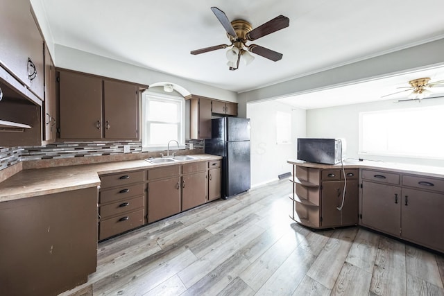 kitchen featuring dark brown cabinetry, sink, backsplash, light hardwood / wood-style floors, and black refrigerator