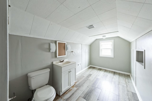 bathroom with wood-type flooring, vanity, toilet, and lofted ceiling