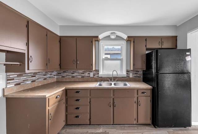 kitchen with decorative backsplash, light wood-type flooring, black fridge, and sink