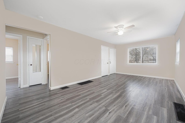 empty room featuring ceiling fan, a healthy amount of sunlight, and dark hardwood / wood-style floors