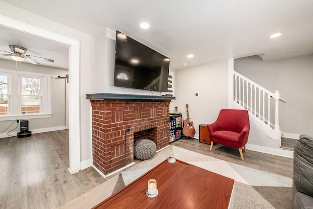 living room featuring ceiling fan, light hardwood / wood-style flooring, and a brick fireplace