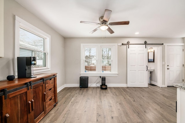 interior space with light wood-type flooring, a barn door, ceiling fan, and a healthy amount of sunlight