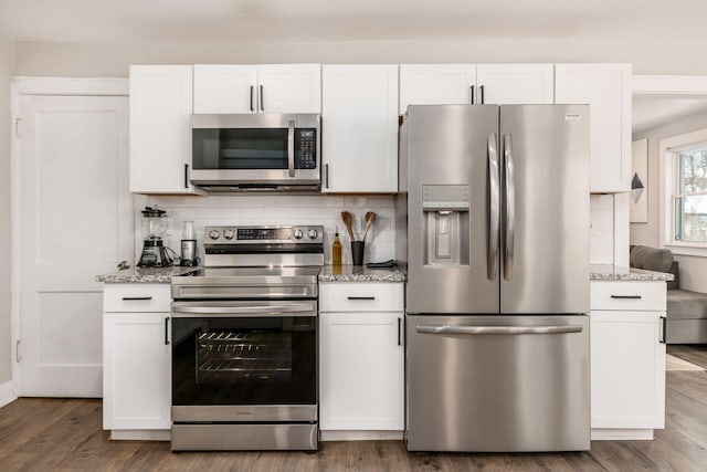 kitchen with hardwood / wood-style flooring, light stone countertops, white cabinetry, and appliances with stainless steel finishes