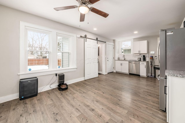 kitchen featuring sink, a barn door, light wood-type flooring, white cabinetry, and stainless steel appliances